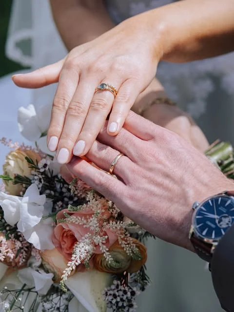 Mains de mariés et leurs bagues au-dessus d’un bouquet de fleurs