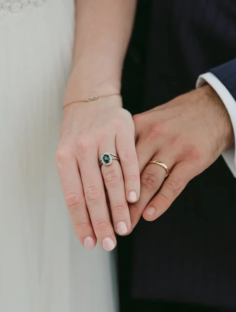 Deux mains réunies portant des alliances et une bague à pierre verte
